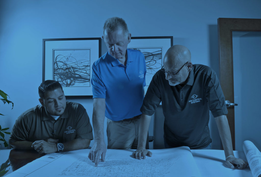 Three male ACS employees review blueprint on table with blue overlay effect